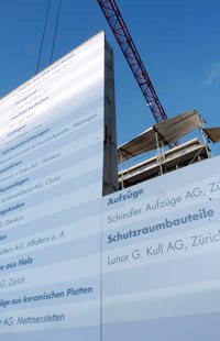 Tafel mit den Namen der beteiligten Architekten und Handwerker, vor einem Neubau